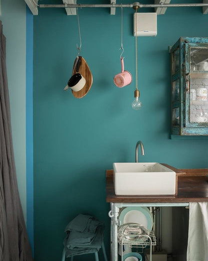 Bathroom with teal walls, white sink, and hanging decorative items.