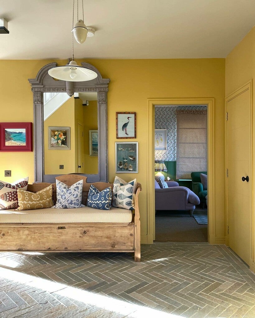 Living room with yellow walls, wooden bench, and decorative pillows.