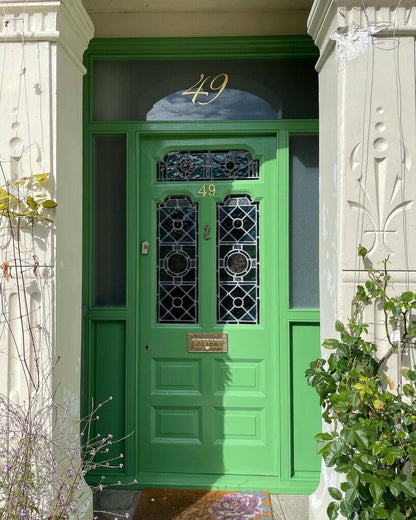 Green door with decorative glass panels and number '49' on a building facade.