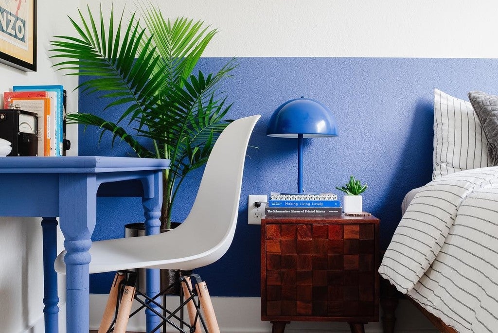 Modern bedroom with blue walls, a white chair, and a blue lamp.