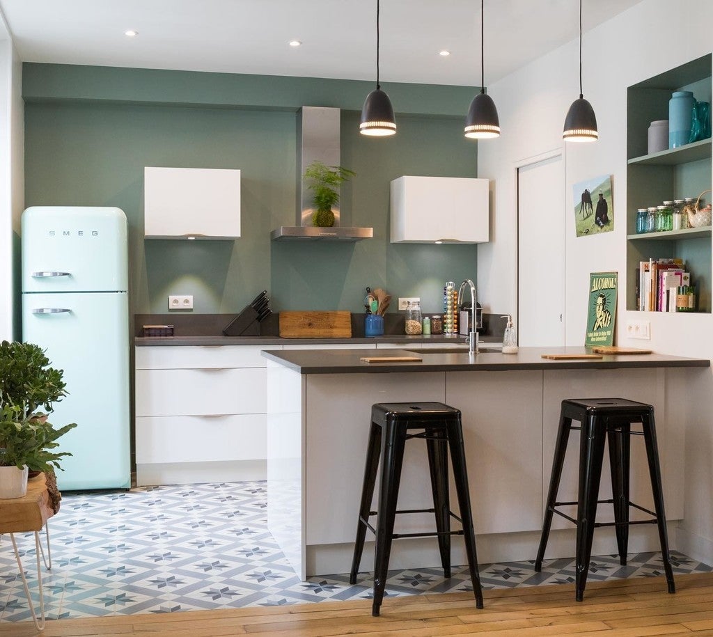 Modern kitchen with teal refrigerator, white cabinets, and black bar stools.