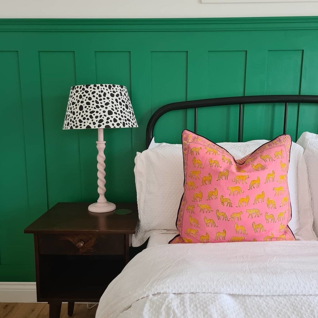 Bedroom with green paneling, a bed with pink and yellow pillow, and a lamp on a nightstand.