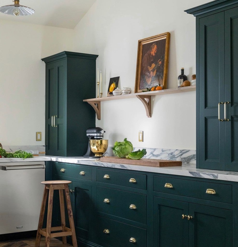 Modern kitchen with dark green cabinets, marble countertops, and a wooden stool.