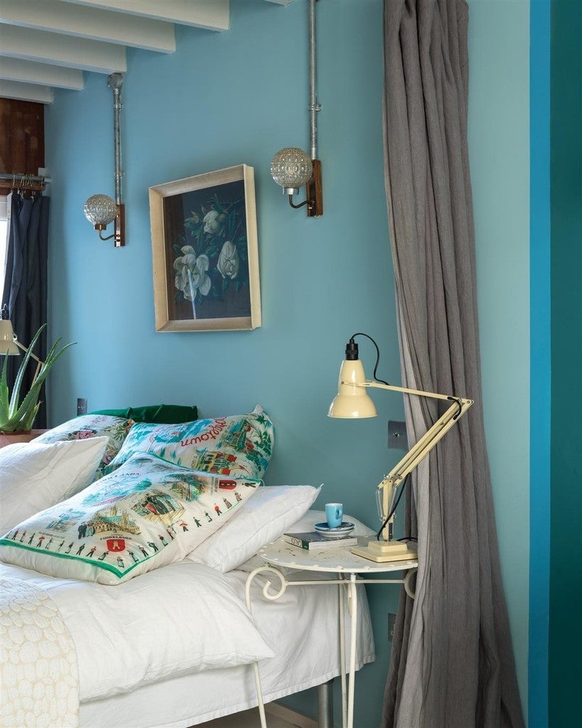 Cozy bedroom with blue walls, a bed with patterned pillows, and a lamp on a nightstand.