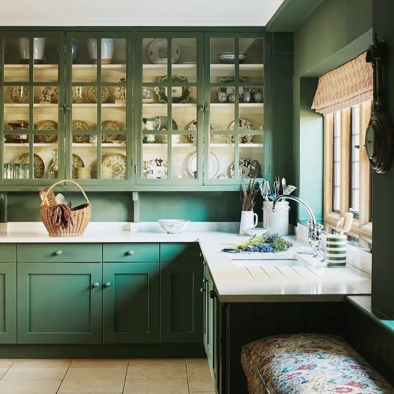 Green kitchen with open cabinets displaying plates and a window with a wicker blind.