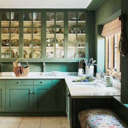 Green kitchen with open cabinets displaying plates and a window with a wicker blind.