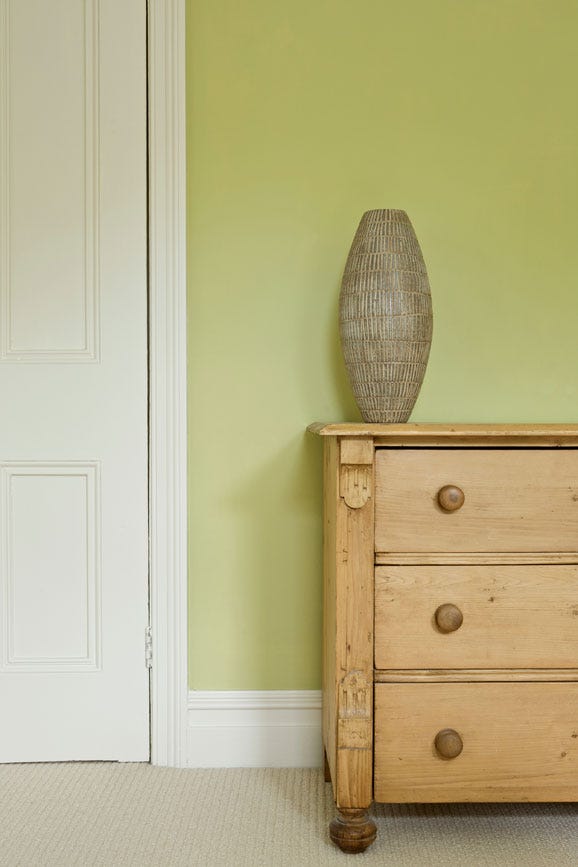 Wooden dresser with a textured vase against a green wall