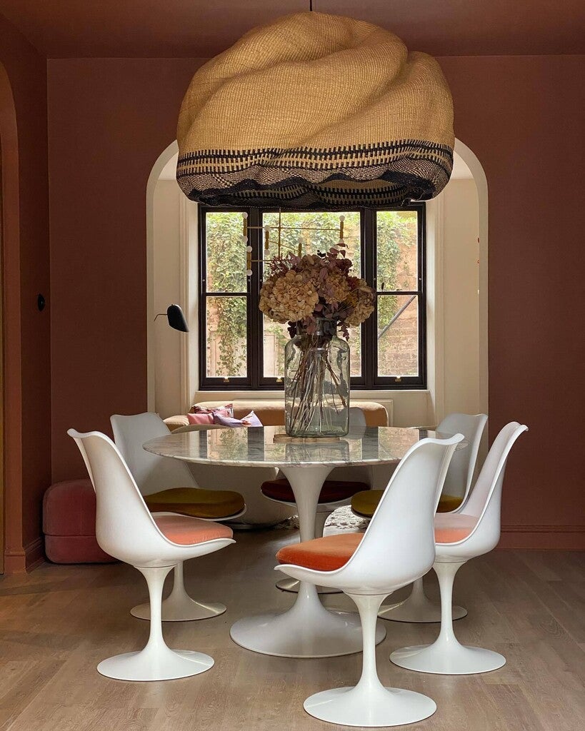 Dining room with a round table and white chairs with orange cushions, featuring a woven light fixture.