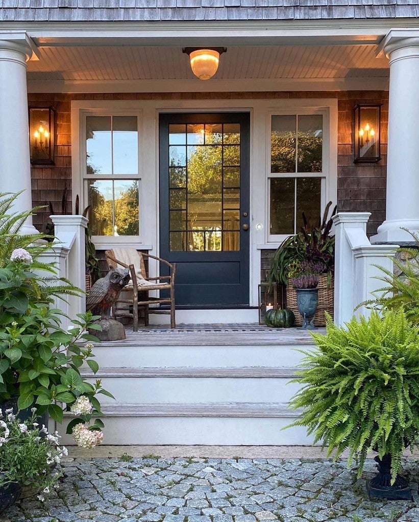 Front porch with a dark glass door, potted plants, and a stone walkway.