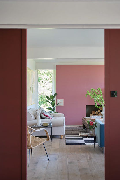 Living room with pink wall and white sofa, viewed through a red door.
