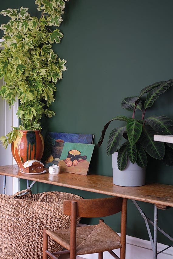 Wooden table with plants and a painting against a dark green wall