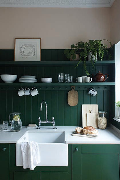 Kitchen with green cabinets, white sink, and various kitchen items on a shelf.