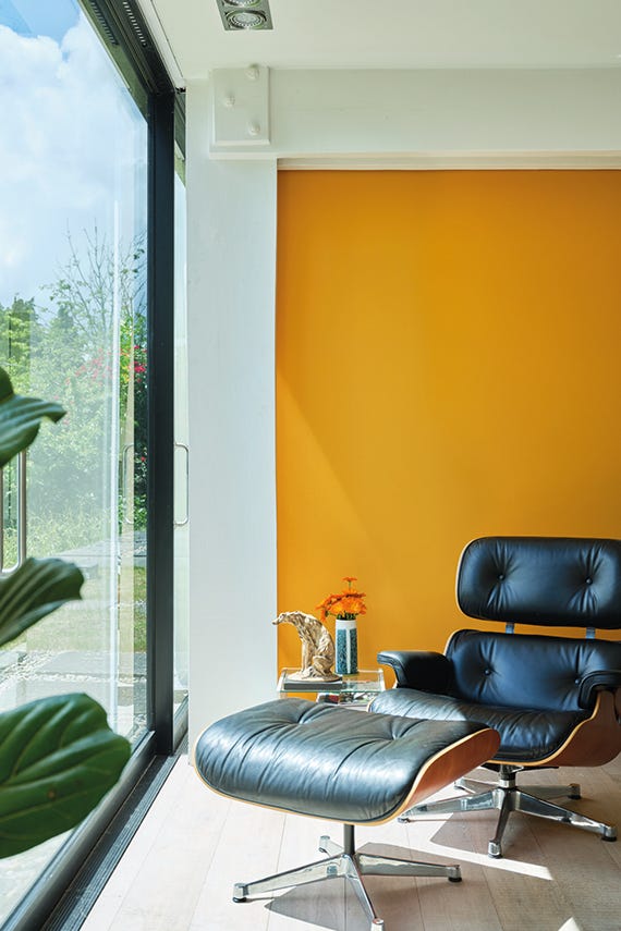 Modern interior with a blue chair and ottoman against a mustard yellow wall.