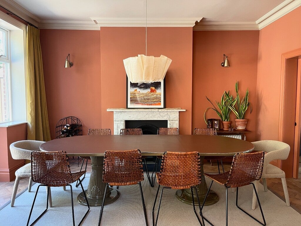 Dining room with a large oval table and wicker chairs against a peach-colored wall.