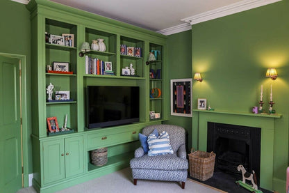 Green living room with bookshelf, TV, and armchair.