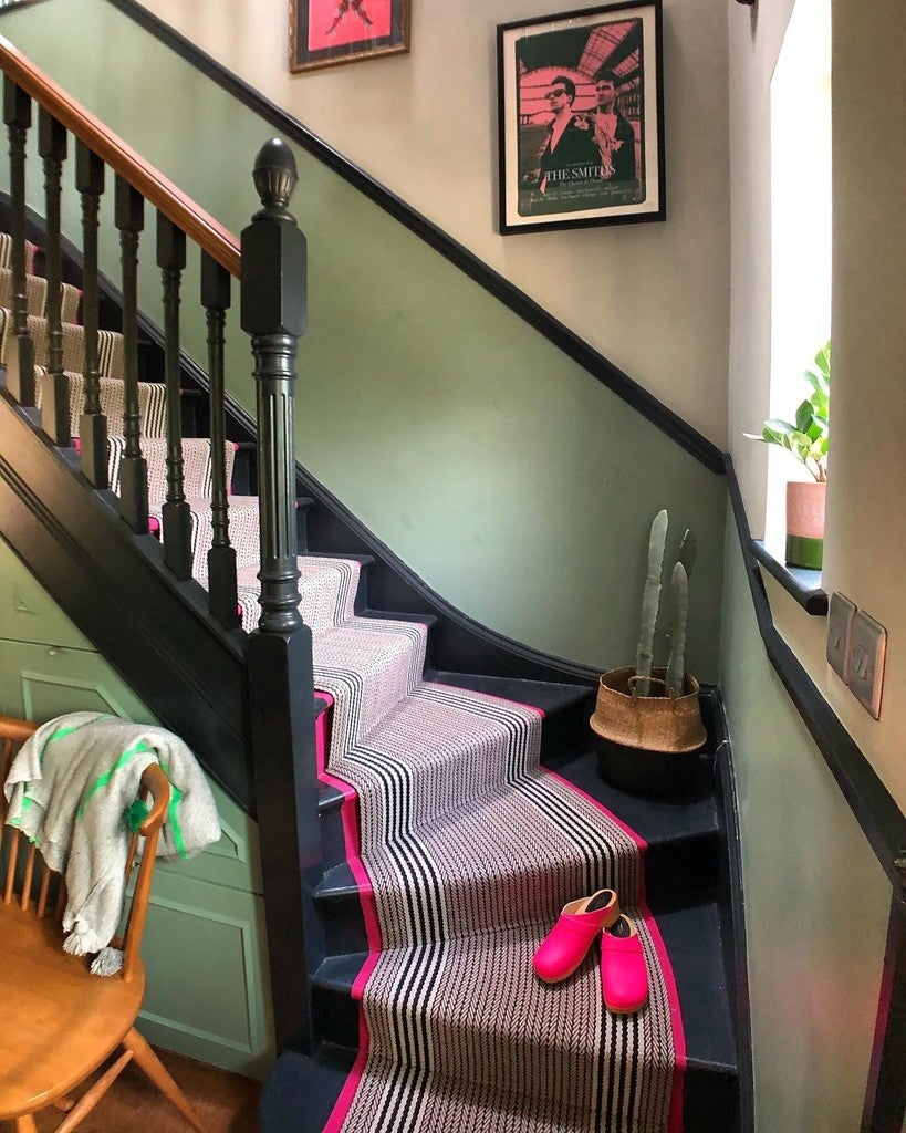 Staircase with a striped runner, pink shoes, and framed pictures on the wall.