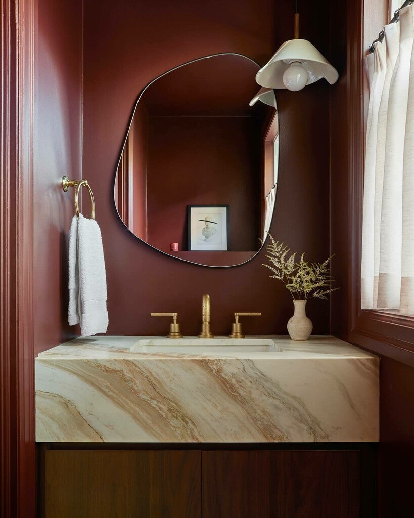 Bathroom vanity with marble countertop, gold fixtures, and a decorative mirror.