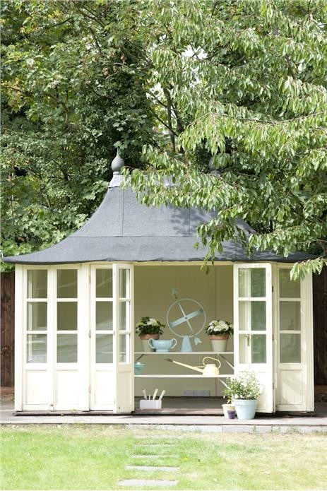 White summerhouse with a gray roof in a garden setting