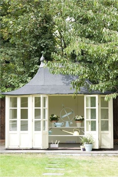 White summerhouse with a gray roof in a garden setting
