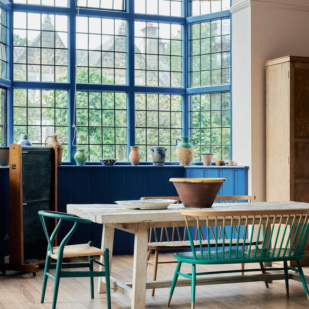 Dining area with wooden table and chairs in front of large windows with a blue wall.