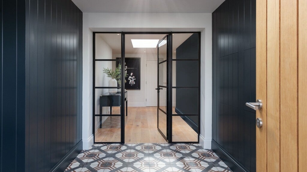 Modern interior with black framed glass doors leading to a room with wooden floor and decor.