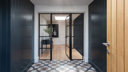 Modern interior with black framed glass doors leading to a room with wooden floor and decor.