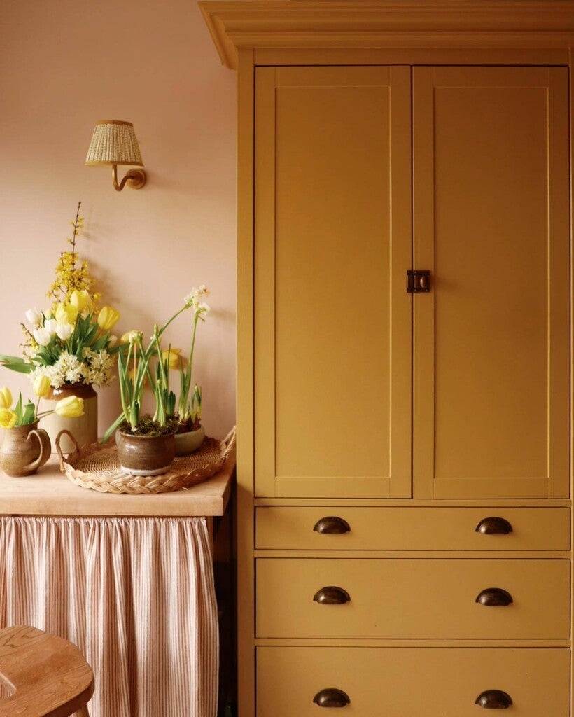 Mustard yellow wardrobe with floral arrangement on a table against a pink wall