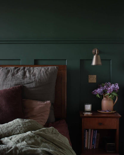 Dark green bedroom with a bed and nightstand featuring a lamp and vase.