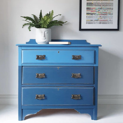 Blue dresser with a plant and framed picture on a white background