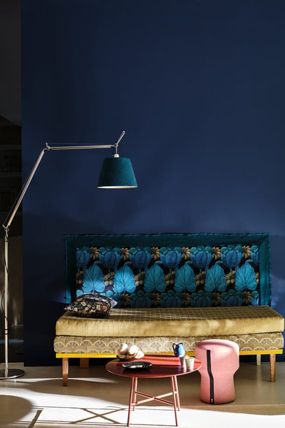 Sofa with decorative cushions against a dark blue wall, illuminated by a floor lamp.
