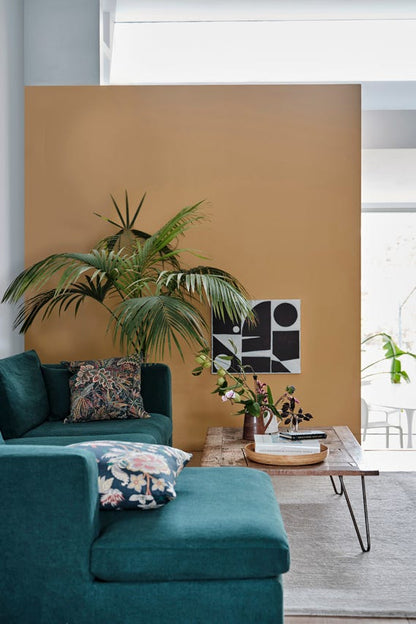 Modern living room with teal sofa, decorative pillows, and a plant against a mustard yellow wall.