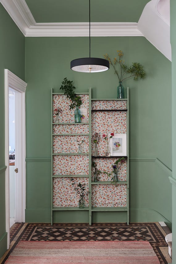 Green bookshelf with floral patterns against a green wall in a room with a patterned rug.