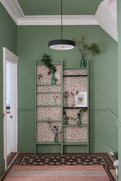 Green bookshelf with floral patterns against a green wall in a room with a patterned rug.