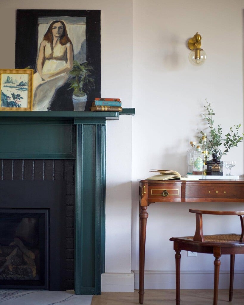 Nestled corner of a room with a green fireplace, wooden desk, and framed artwork.
