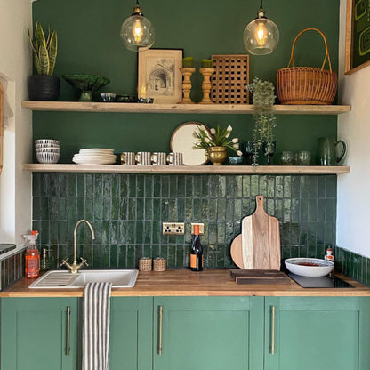 Kitchen with green tiled backsplash, wooden countertops, and shelves with decorative items.