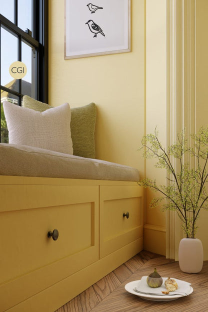 Yellow window seat with cushions, a plant, and a plate of cookies in a room with yellow walls.