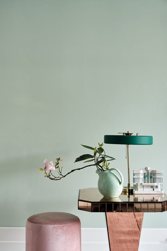 Decorative table with a lamp, vase, and plant against a light green wall.