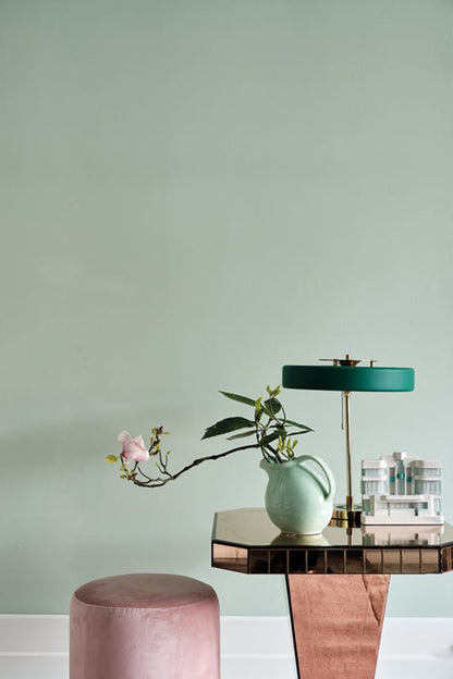Decorative table with a lamp, vase, and plant against a light green wall.