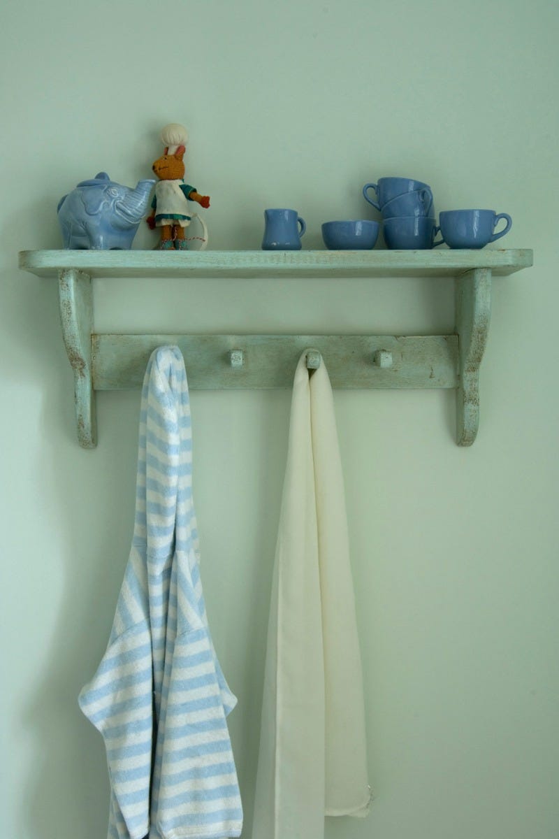 Shelf with decorative items and hooks with cloths against a light green wall