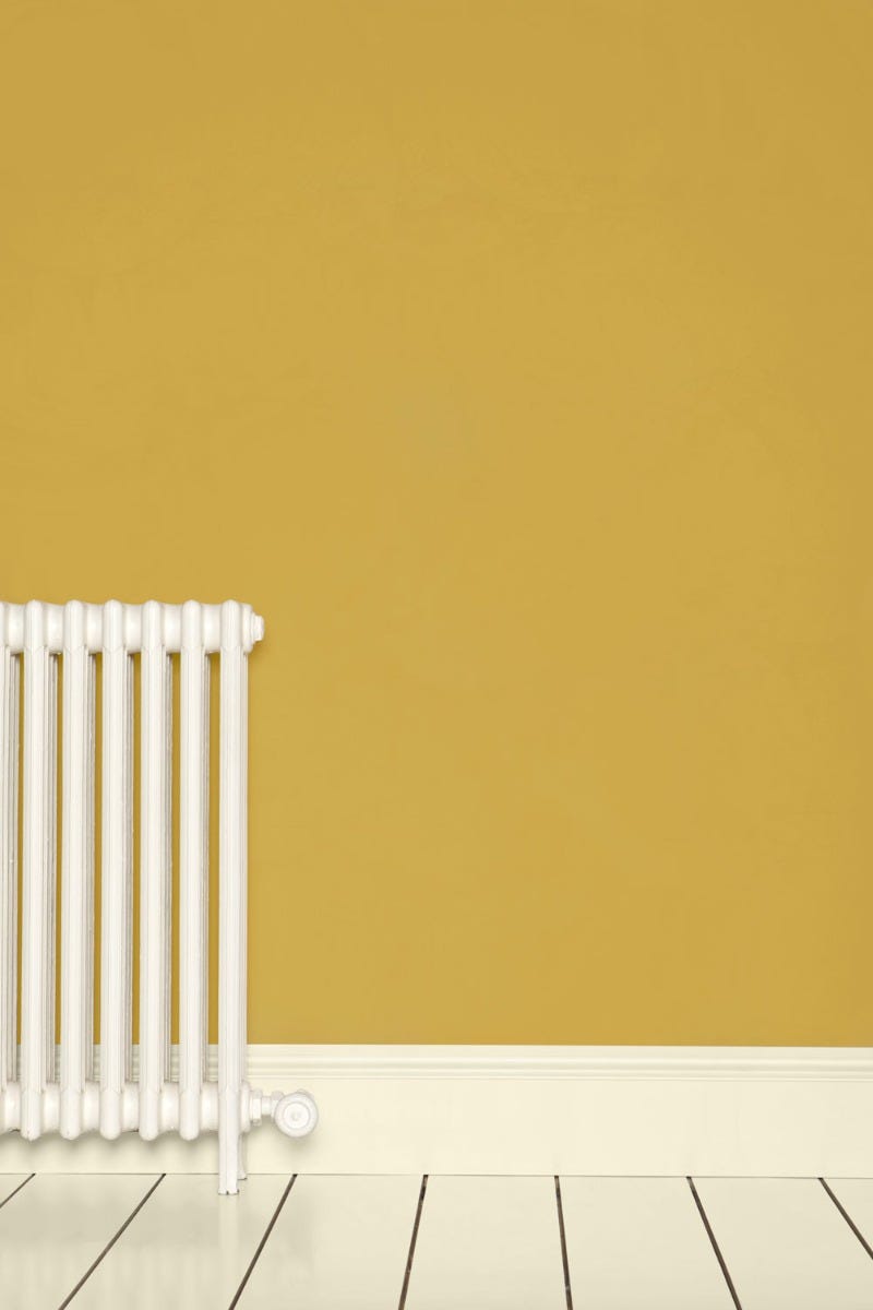 White radiator against a mustard yellow wall with a white floor.