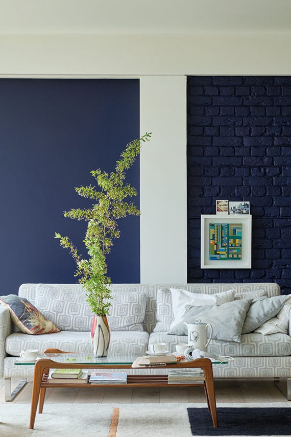 Modern living room with a white sofa, decorative pillows, and a plant against a dark blue wall.