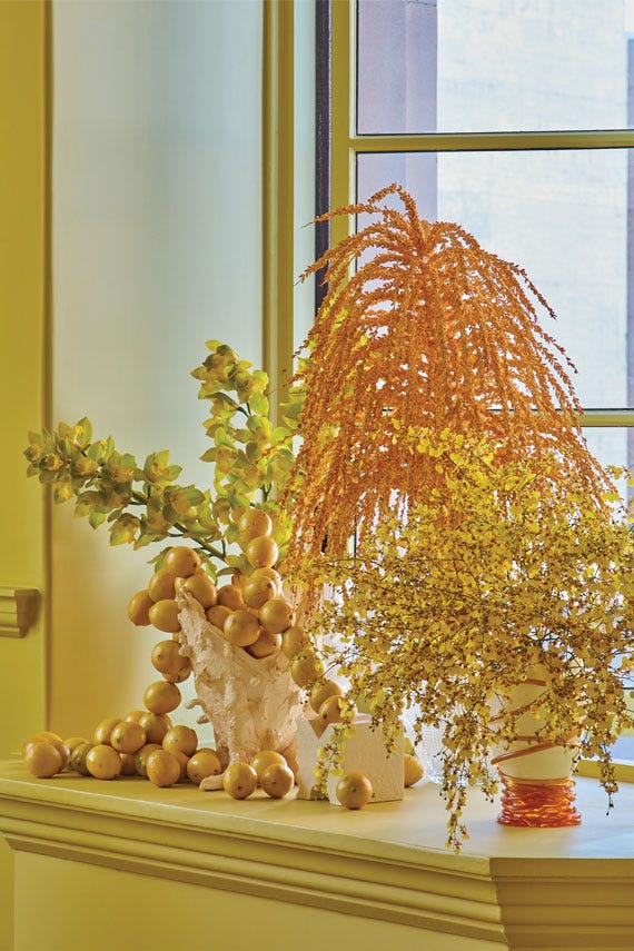 Decorative display on a mantelpiece with fruits, flowers, and a vase.