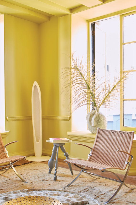 Modern interior with wicker chairs, a small table, and decorative elements against a yellow wall.