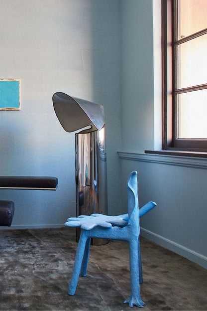 Modern interior with a blue chair, metallic lamp, and abstract painting.