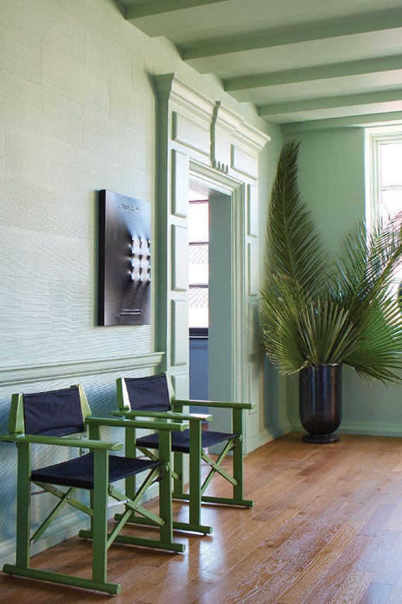 Green chairs with black cushions in a room with white walls, a plant, and a painting.