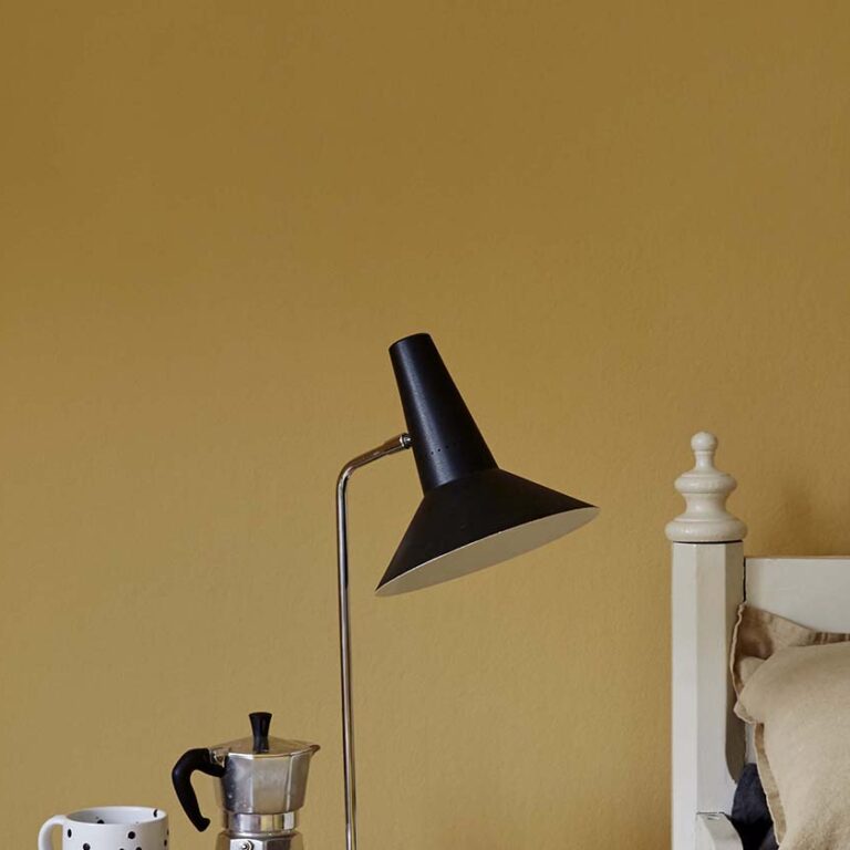 Black floor lamp against a mustard yellow wall with a coffee maker and mug on a surface.