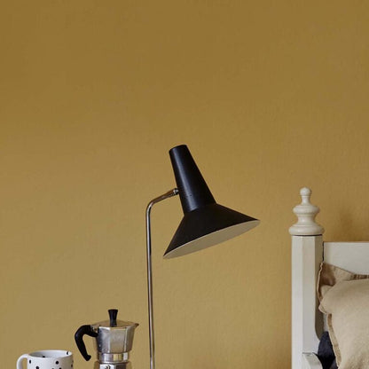 Black floor lamp against a mustard yellow wall with a coffee maker and mug on a surface.